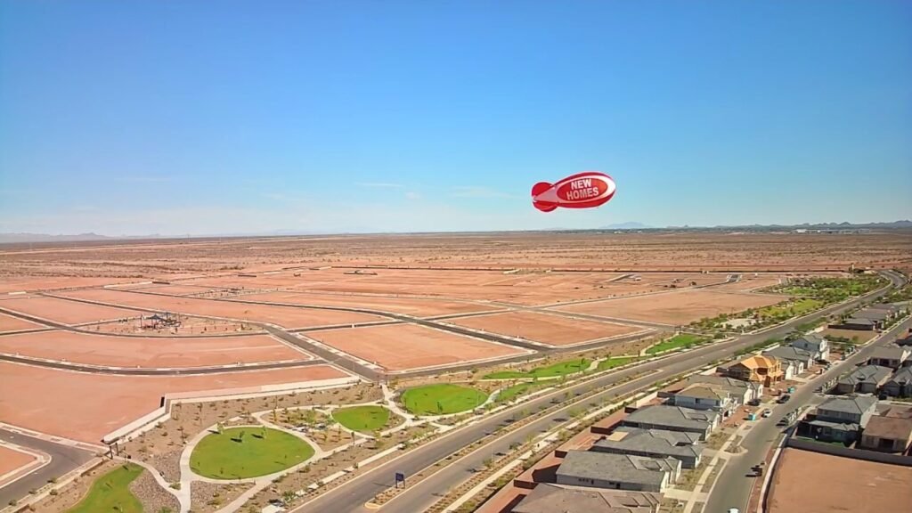 Red and white NEW HOMES advertising blimp flying above a new housing development